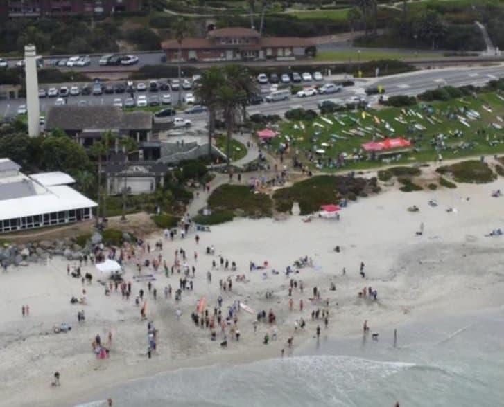 Aerial view of Del Mar's Powerhouse Park and beach with event tents and paddleboards laid out on the grass.
